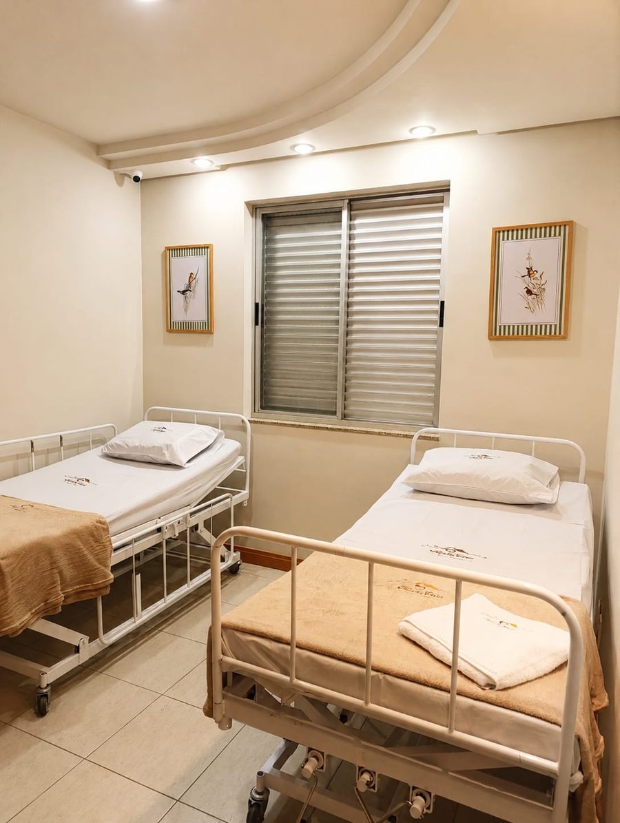 Quarto compartilhado com duas camas articuladas, grades de proteção laterais e câmera de monitoramento no teto.