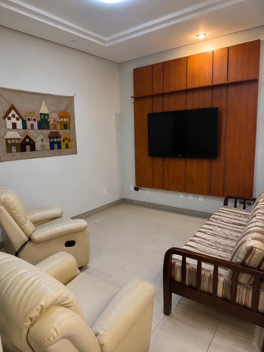 Sala de estar com poltronas reclináveis, sofá de madeira, televisão em painel de madeira e um painel de tecido com casinhas coloridas na parede.